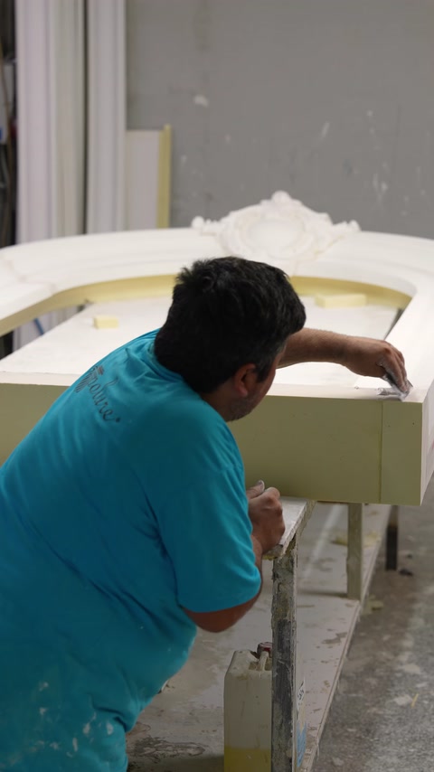 Un artigiano leviga la superficie di un pezzo di modanatura architettonica curva