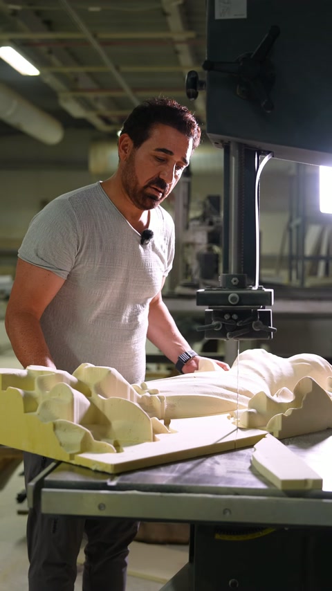 A craftsman examines carved bridal relief components beside workshop machinery.