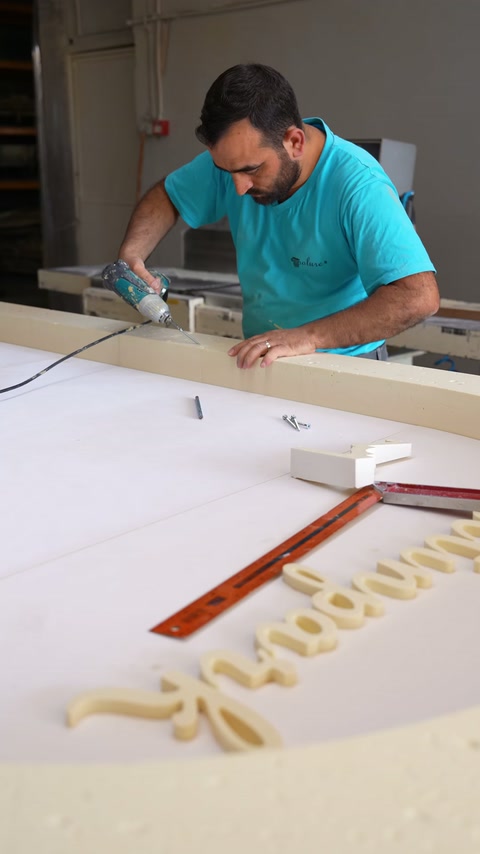 Worker trims polyurethane components on a bench beside decorative lettering.