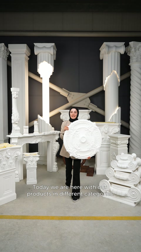 A large ceiling rose is presented by the presenter in front of classical columns.