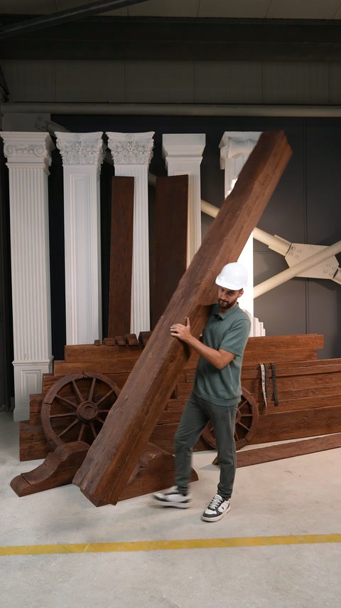 Un operaio sostiene una trave decorativa effetto legno inclinata accanto a componenti decorativi impilati