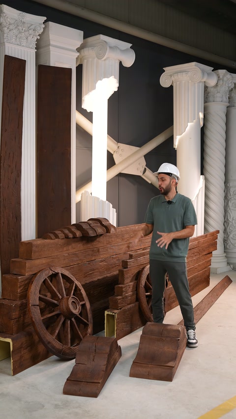 Il presentatore indica travi rustiche stratificate e campioni da pavimento nelle vicinanze