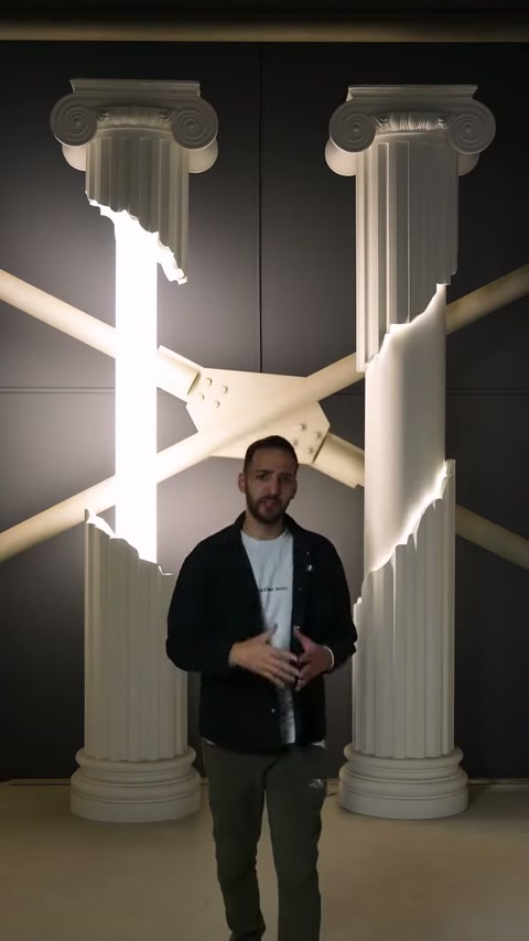 Presenter stands centered beneath geometric lighting between decorative showroom columns.
