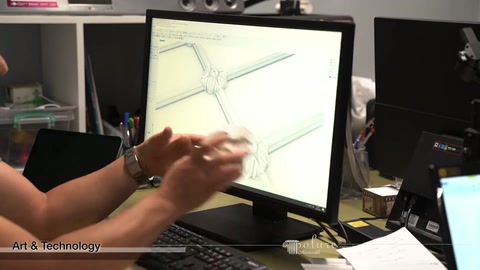 Small assembly connector piece held toward screen while technical drawing displayed