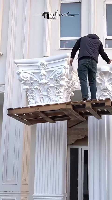 A square Corinthian capital is moved into installation position on scaffolding
