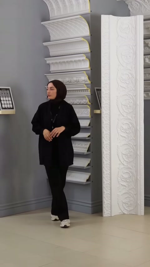 Sunucu, duvar raflarındaki klasik desenli kartonpiyerleri inceleyerek anlatıyor.