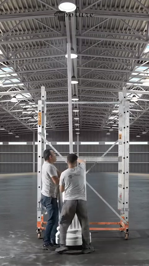 Gli operai mantengono in posizione verticale il lungo elemento della colonna davanti alla struttura.