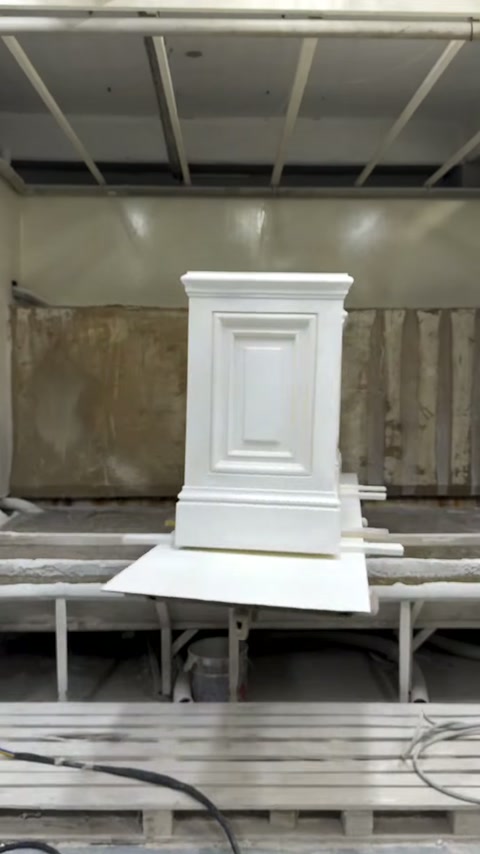 Finished white paneled pedestal rests inside the spray-finishing booth.