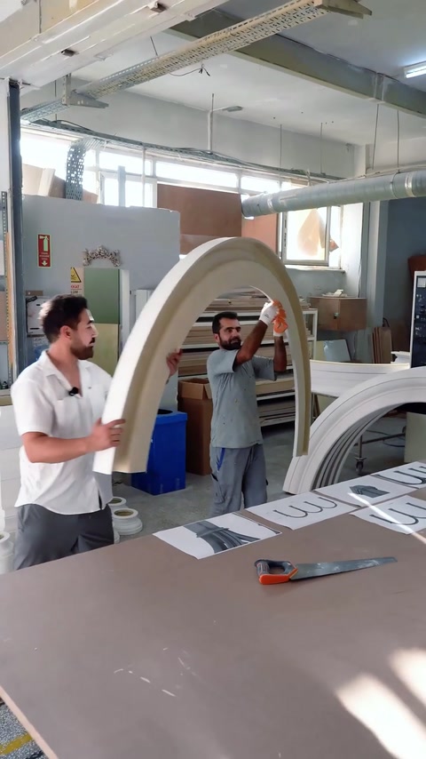Due operai che sollevano un grande modulo d'arco bianco all'interno del laboratorio
