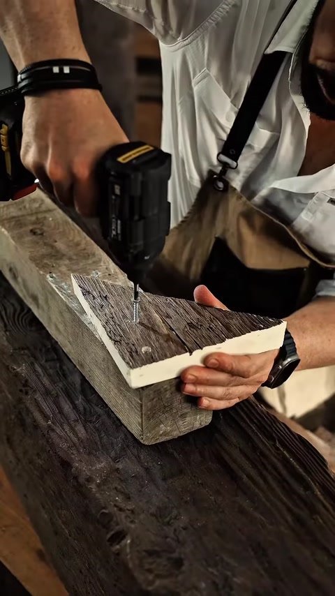 Un elemento di profilo effetto legno viene fissato al banco da lavoro con un trapano.