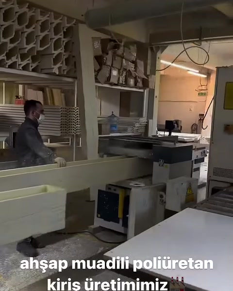 Un operaio guida un lungo profilo di trave in poliuretano nella macchina di produzione