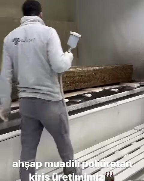 Un operaio applica il colore con una pistola sulla superficie della trave con texture legno