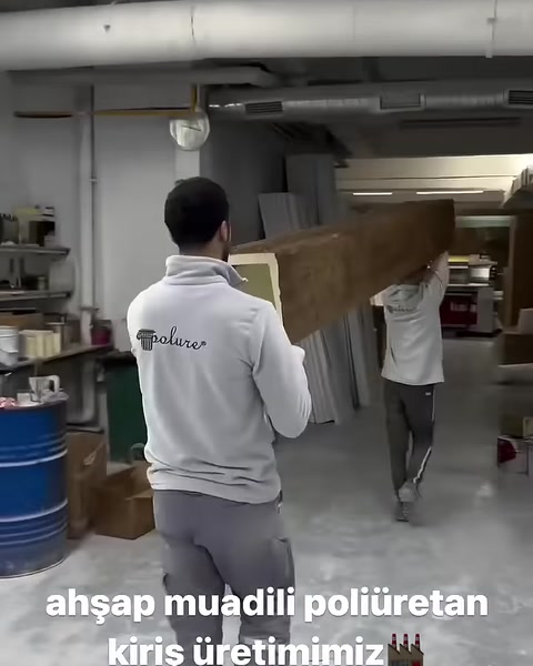 Due operai trasportano insieme una lunga trave con texture legno