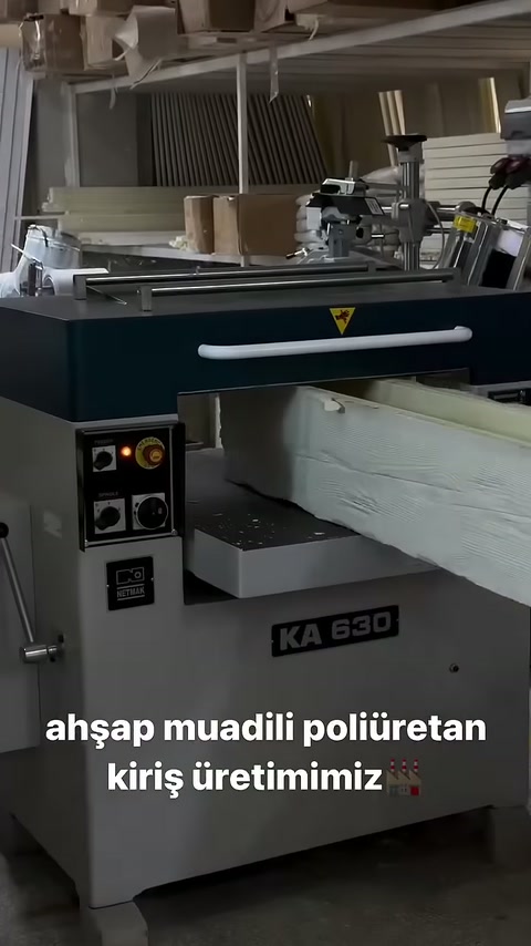 La trave di colore chiaro è in attesa sul piano di alimentazione della macchina di profilo.