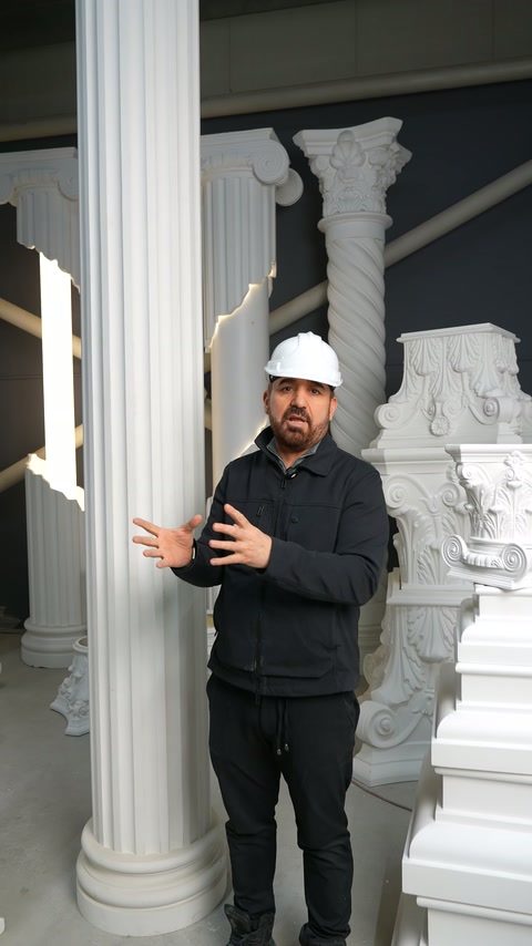 Sunucu, dekoratif sütunların arasında elindeki numuneyi kameraya sunuyor.