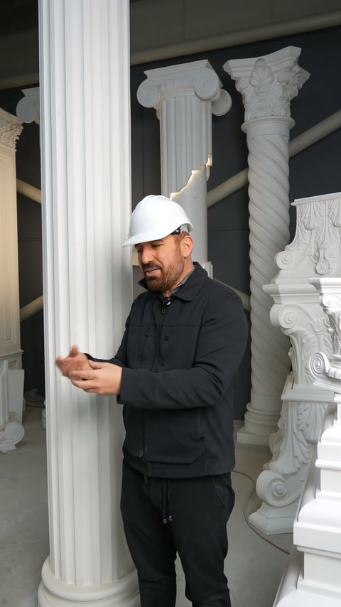 İşlemeli sütun başlıklarının önünde sunucu iki eliyle anlatım yapıyor.