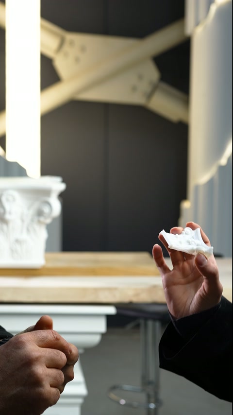 Un piccolo dettaglio di capitello bianco viene tenuto tra le dita in laboratorio