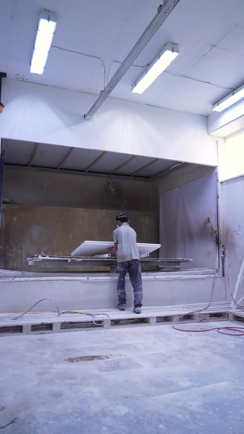 Operaio che sposta un piano attraverso la cabina di verniciatura a spruzzo