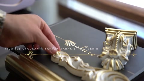 El, altın profillerin yanındaki açık renkli kıvrımlı motife uzanıyor.