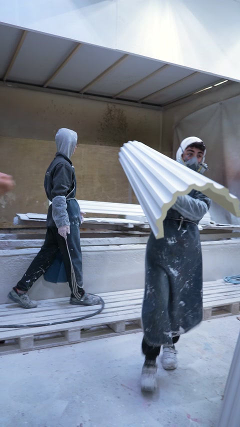 Workers carry a long decorative cornice through the workshop