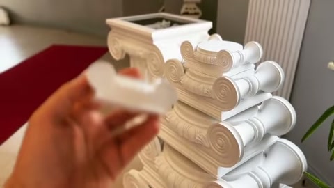 Volute column capitals are arranged while another decorative piece is held in hand.