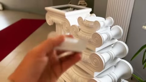 A decorative accessory piece is rotated and examined in front of stacked column capitals.