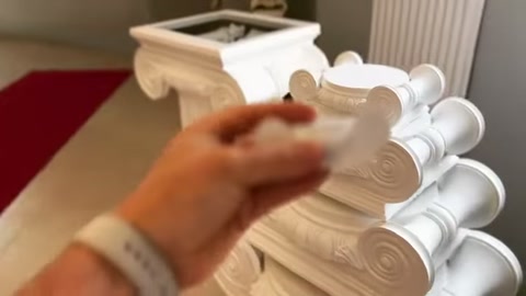 A white ornamental piece held in hand is brought closer to the upper section of a capital.