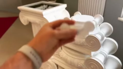 A small decorative element is held over a volute capital before placement.