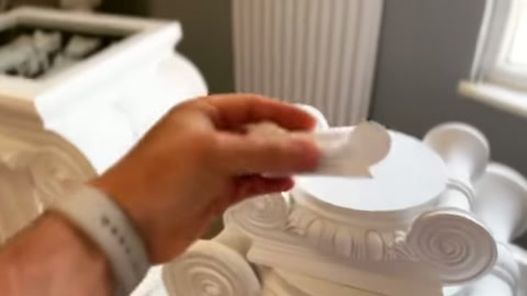 A hand prepares to place a small ornament at the upper center of a capital.
