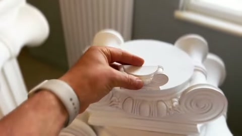 A hand gently positions the installed decorative piece on the capital.