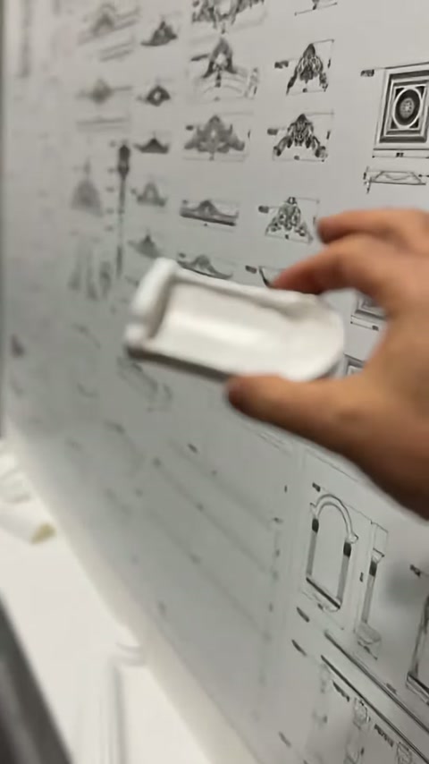 Il pezzo decorativo sopra la cornice viene tenuto in mano davanti ai disegni tecnici del prodotto
