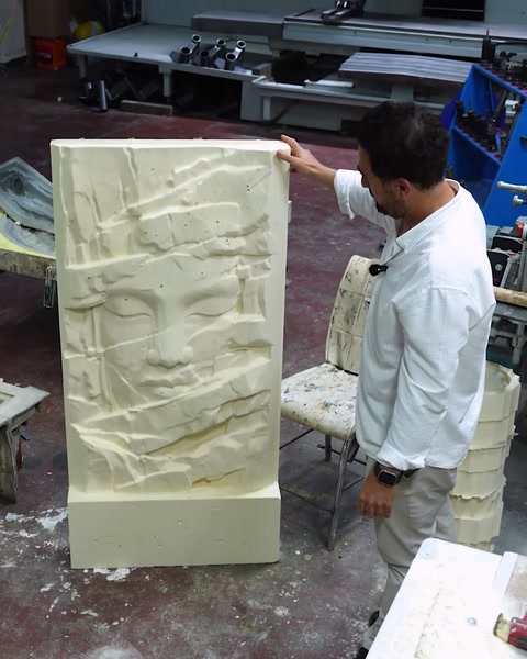 L'operaio maneggia un elemento decorativo curvo accanto al pannello a rilievo