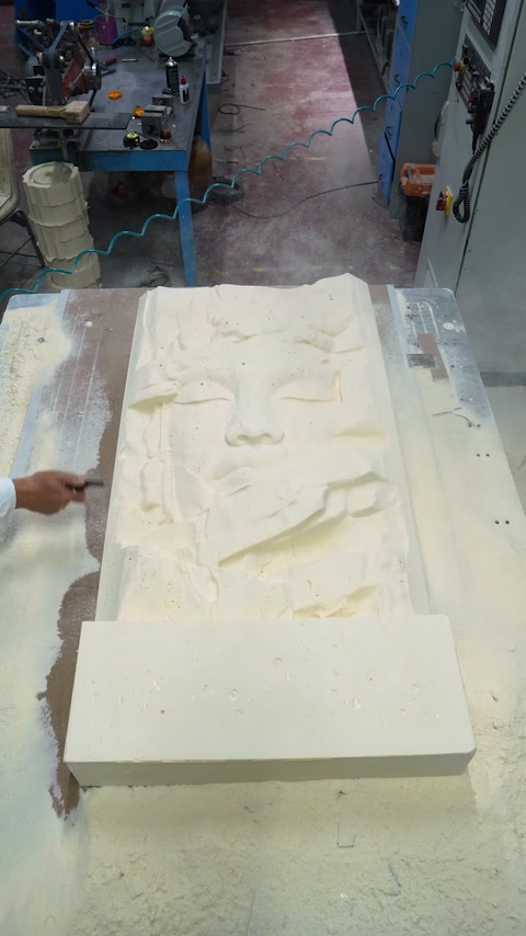 Worker inspects the large carved relief panel on the workshop table