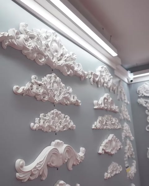 Sulla parete espositiva sono disposti modelli di frontoni decorativi bianchi in forme diverse.