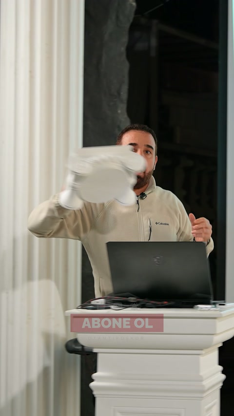 Sunucu, beyaz dekoratif başlık parçasını göğüs hizasında tutarak anlatıyor.