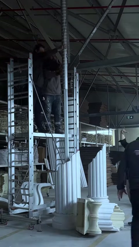 Due artigiani fissano il fusto della colonna alta sul pavimento del laboratorio.