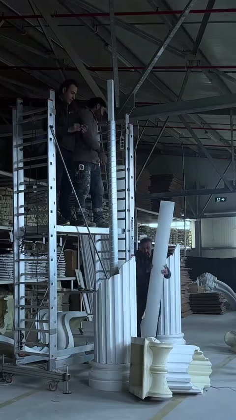 Il fusto della colonna in poliuretano viene sollevato da due artigiani per il montaggio.