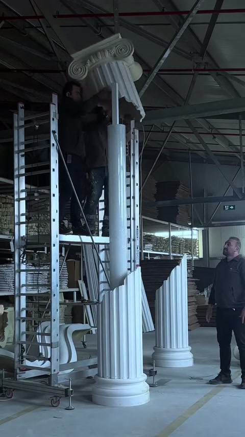 La parte superiore della colonna con capitello ionico viene bilanciata da due artigiani.