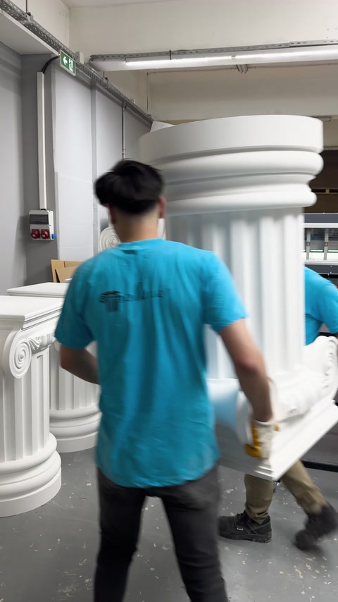 Workers carry a large decorative column through the production facility.