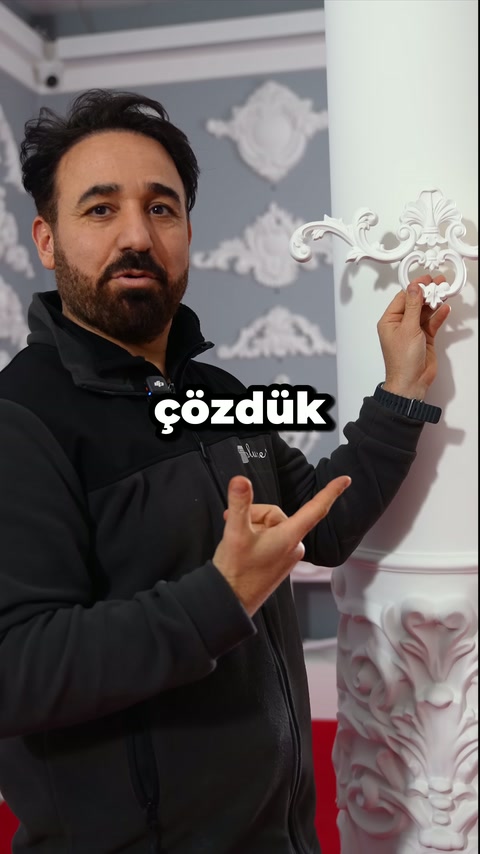 A craftsman points to and presents a curved ornamental element beside the column.