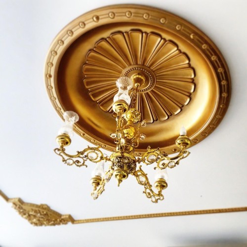 Cupola dorata in poliuretano e lampadario classico per ville eleganti <h2>Decorazione classica con cupola dorata</h2><p>Una cupola da soffitto in <strong>poliuretano</strong> con finitura dorata rappresenta una soluzione decorativa raffinata per interni di ville classiche. La superficie mostra scanalature radiali che ricordano motivi tipici dell’arte neoclassica, irradiandosi verso l’esterno in modo equilibrato. Il bordo circolare, punteggiato da piccoli rilievi geometrici, conferisce al soffitto un aspetto armonioso e solenne.</p><h2>Armonia di forme e dettagli</h2><p>Al centro della composizione è sospeso un lampadario con delicati elementi floreali dorati e bracci riccamente intagliati. Le decorazioni curvilinee richiamano lo stile barocco, mentre le gocce di cristallo captano e diffondono la luce in maniera suggestiva. Questa combinazione tra il metallo lucente e la cupola dorata crea un’atmosfera regale, perfetta per ambienti dedicati all’accoglienza e alla rappresentazione.</p><h2>Storia e ispirazione</h2><p>Le cupole e i rosoni decorativi hanno un’origine antica, spesso impiegate nell’architettura rinascimentale e barocca come elementi di centralità visiva. Qui, il materiale moderno in <strong>poliuretano</strong> sostituisce il gesso tradizionale, garantendo durabilità pur mantenendo l’eleganza tipica delle lavorazioni storiche.</p><ul><li>Motivi radiali e geometrici in rilievo</li><li>Finitura <strong>dorata</strong> che valorizza la luce</li><li>Lampadario con dettagli classici e cristalli</li><li>Ideale per ville e residenze eleganti</li></ul>

<p>Una cupola dorata in poliuretano esalta la raffinatezza di un soffitto classico. Le sue linee radiali creano un ritmo preciso e armonioso. Il bordo circolare con motivi geometrici aggiunge profondità ed eleganza. Al centro, un lampadario arricchito da cristalli diffonde luce morbida. I dettagli floreali dorati richiamano lo splendore barocco. L’insieme comunica un gusto aristocratico e senza tempo. In una villa elegante questo elemento diventa un fulcro visivo. La resistenza del <strong>poliuretano</strong> garantisce durata e qualità. La finitura <strong>dorata</strong> amplifica il prestigio complessivo. Le scanalature radiali ricordano tradizioni architettoniche neoclassiche. Un lampadario curvilineo completa la scena decorativa. L’atmosfera che ne deriva è calda e suggestiva. Il gioco di luce valorizza ogni dettaglio dorato. Questo tipo di decorazione è perfetto per sale di rappresentanza. Il connubio tra innovazione e tradizione rende lo stile unico.</p>