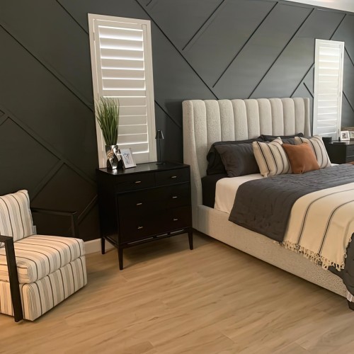 Modern classic bedroom with polyurethane wall panel details <h2>Modern Classic Bedroom Design</h2><p>This bedroom embraces the essence of the <strong>modern classic</strong> style by balancing geometric precision with timeless comfort. The key design feature is the wall decorated with <strong>polyurethane</strong> trims that form sharp diagonal lines, creating a distinctive contrast against the smooth dark surface. Such wall treatments not only add personality but also generate rhythm and symmetry in the space.</p><p>The upholstered headboard, with its vertical channel design, contrasts gently with the angular backdrop. The use of <strong>wooden flooring</strong> in a light tone brings warmth and balance, making the space inviting. In contrast, sleek black nightstands with metallic hardware add a grounding effect and reinforce the classic color scheme.</p><p>Window shutters in clean white act as stylistic focal points, framed neatly like sculptural inserts within the patterned wall. The balance of soft fabrics, detailed textures, and structured geometry ensures the room maintains its refined atmosphere.</p><h2>Historical Note</h2><p>The use of trim in interior decoration has its roots in classical architecture, where moldings and panels were employed to give depth and ornamentation to walls. This practice has been modernized through <strong>polyurethane</strong> elements, allowing designers to achieve high precision with lightweight and durable materials.</p><h2>Key Elements</h2><ul><li>Diagonal <strong>geometric patterns</strong> in polyurethane trim</li><li>Soft neutral upholstered bed with textured detailing</li><li>Contrasting black furniture with metallic subtleties</li><li>Striped textiles introducing subtle linear harmony</li><li>Bright white shutters cutting through the dark backdrop for balance</li></ul>

<p>This modern classic bedroom demonstrates a harmonious balance of clean lines and timeless details. The dark feature wall uses <strong>polyurethane</strong> trim to form diagonal patterns that introduce depth. The upholstered headboard softens the geometric strength of the wall. Light <strong>wooden flooring</strong> brings warmth and continuity to the space. Black nightstands anchor the room with a bold contrast. Crisp white shutters punctuate the dramatic background, offering symmetry and brightness. The use of layered textiles enriches the overall design. A striped armchair ties together linear and fabric motifs effectively. The diagonal <strong>geometric patterns</strong> act as a visual rhythm. The neutral color palette keeps the composition balanced. Subtle metallic accents highlight refinement. Historical paneling traditions are reinterpreted with modern materials. Texture contrast between hard trim and soft bedding enhances comfort. The arrangement of furniture maintains flow and proportion. This blend of precision and comfort reflects the essence of modern classic design.</p>