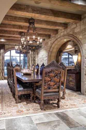 Rustic Classic Living Room with Polyurethane Beams and Ornamental Details <h2>Rustic Charm and Classic Elegance</h2><p>The living room captures the essence of a <strong>rustic</strong> yet classic style through the seamless fusion of natural textures and refined details. Polyurethane beams across the ceiling mimic the sturdiness of heavy timber while offering durability and ease of maintenance. These architectural elements create a warm and inviting atmosphere by drawing the eye upward and framing the stone walls.</p><p>The combination of textured stone surfaces and finely carved wooden furniture reflects a balance between authenticity and ornamentation. The chairs surrounding the table feature detailed motifs, ornamental perforations, and leather-like inlays, showcasing the artistry behind traditional woodworking styles. Their backs present symmetrical designs and carefully engraved flourishes that echo the grandeur of historic interiors.</p><h2>Color Palette and Textural Harmony</h2><p>The color scheme consists of earthy browns, muted grays, and golden tones that enhance the sense of calm and sophistication. Plush patterned rugs with intricate motifs tie the entire composition together, adding color depth and softness underfoot. Subtle floral and geometric accents on the textiles complement the surrounding stone and wood, establishing textural harmony within the room.</p><p>Decorative iron chandeliers contribute to the visual rhythm of the ceiling, their circular frames echoing the geometry of the arched stone niche and the large arched window. These light fixtures cast a gentle glow, emphasizing both the detailed <strong>ornamentation</strong> and the serene ambiance within the living space.</p><h2>A Subtle Historical Note</h2><p>Rustic interiors often borrow cues from medieval and renaissance architecture, particularly in the use of vaulted arches and natural stone. The arched niche with its framed mirror recalls such historical references, subtly grounding the design in a lineage of European classical spaces while remaining practical and intimate for modern living.</p>

<p>This rustic classic living room blends natural stone, <strong>polyurethane beams</strong>, and hand-carved wood to create timeless appeal. The detailed chairs with ornamental motifs contribute to a feeling of historic artistry. A richly patterned carpet provides warmth and visual movement across the floor. Heavy wooden slopes of the furniture emphasize craftsmanship. Elegant <strong>wrought-iron chandeliers</strong> suspend over the table, offering soft illumination. The arched stone niche with a framed mirror adds architectural depth. Warm brown and golden hues dominate the palette. Balanced use of <strong>textures</strong> enhances harmony in the room. Intricate floral and geometric rug patterns tie the ensemble together. Refined <strong>details</strong> highlight the classical aesthetic. The room maintains both comfort and grandeur. Stone walls lend solidity and rustic charm. Ceiling beams create vertical strength and continuity. Every furnishing detail supports unity of design. The overall composition achieves elegance while preserving traditional authenticity.</p>